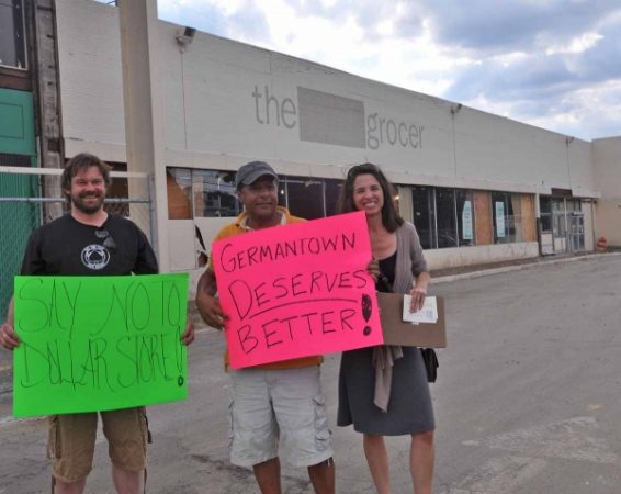 From left, Geir Overland, Pedro Rodriguez, and Donna Uettwiller hold signs on the sidewalk in front of Chelten Plaza. (Kristen Mosbrucker/for NewsWorks)