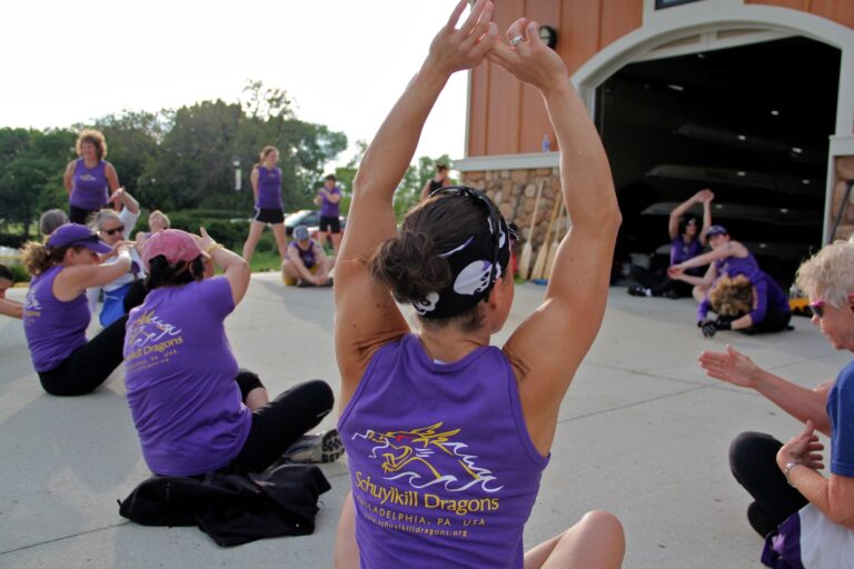 The Schuylkill Dragons stretch behind the Camden County Boathouse before a practice on the Cooper River. (Emma Lee/for NewsWorks)