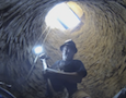 a man holding a shovel at the bottom of a deep pit
