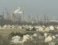 a chemical plant towers behind a group of houses