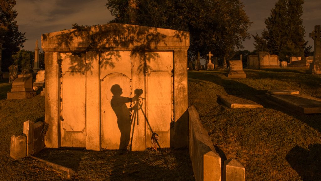 1SODIUM VAPOR A photographer's shadow is cast against the wall of a mausoleum from the illumination of street lights. (Jonathan Wilson for Newsworks)