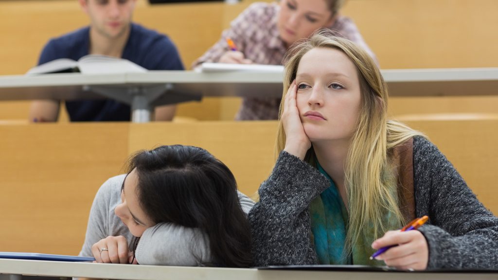 Demotivated students sitting in a lecture hall with one girl napping in college
