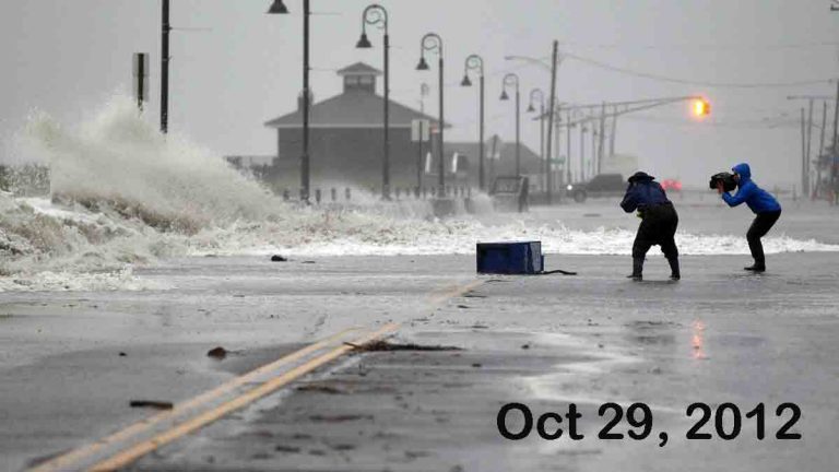 People photograph as rough surf of the Atlantic Ocean breaks over the beach and across Beach Ave.