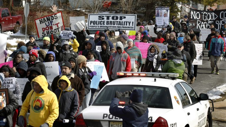 People hold signs and shout as they march in protest of a recent fatal police shooting Saturday