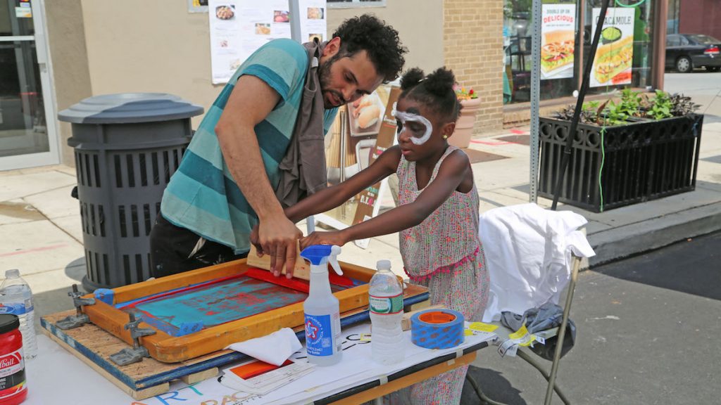 3-4 Jianni (L) and Manny Gonzales from Manayunk Roxborough Art Center pressing a custom printing on a T-shirt (Natavan Werbock/for NewsWorks)