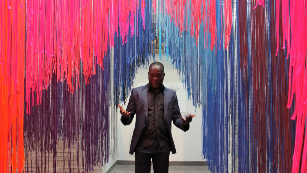Architect Francis Kéré beckons visitors into into an installation that represents both Philadelphia and his home village of Gando in Burkina Faso. Hanging paracute cords create enclosures and recorded sounds from both locations play softly. (Emma Lee/WHYY)