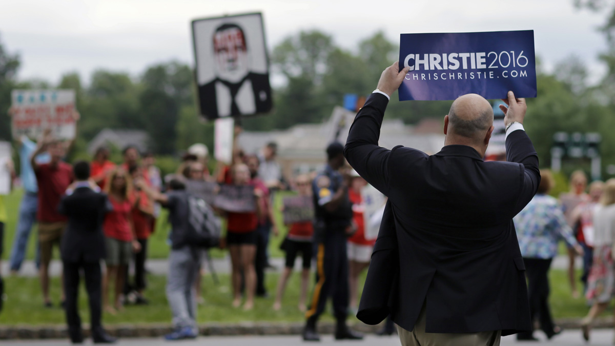  A man holds up a Christie for president sign as he passes a group of protesters after Christie announced that he is running for the Republican nomination for president Tuesday at Livingston High School in Livingston, New Jersey. (AP Photo/Mel Evans) 
