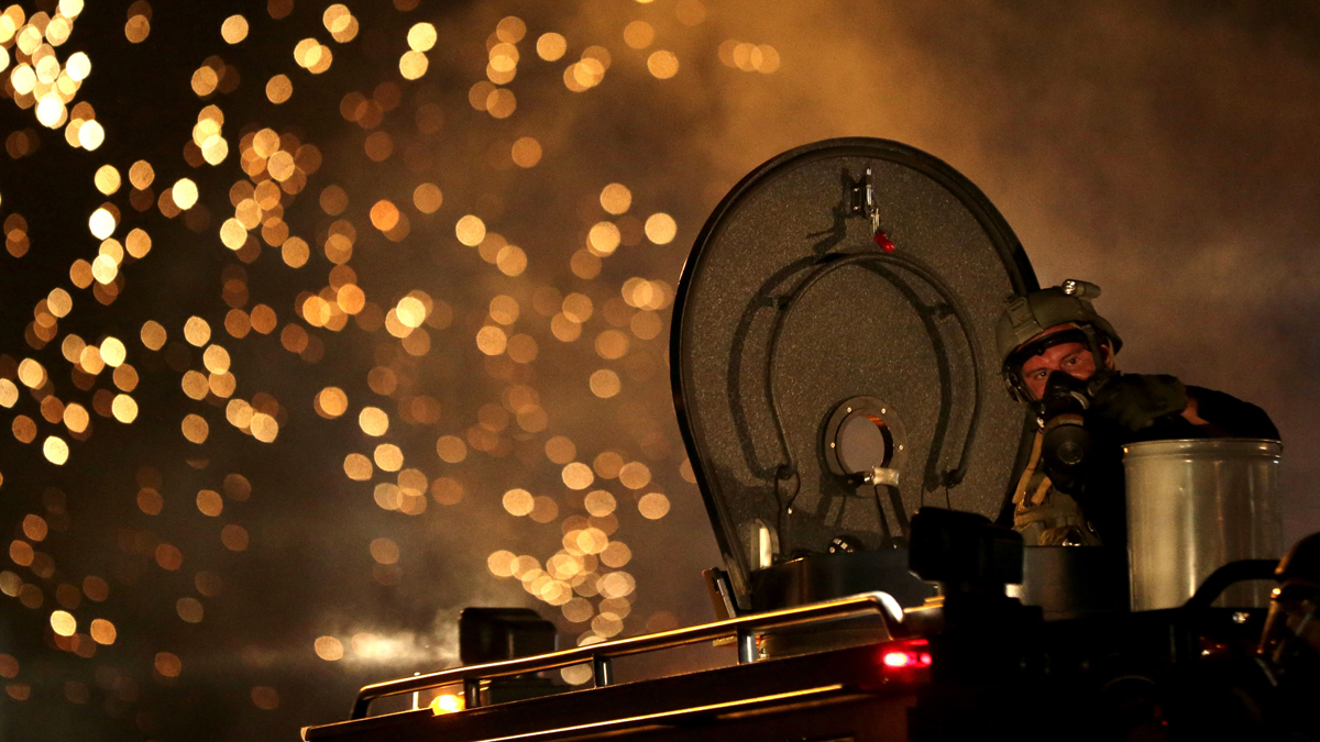   FILE - In this Aug. 17, 2014 file photo, a law enforcement officer watches from an armored vehicle after a device was fired to disperse a crowd during a protest for Michael Brown, in Ferguson, Mo. The response to Brown’s death turned violent because of a convergence of factors, observers said. (Charlie Riedel/AP Photo, file) 