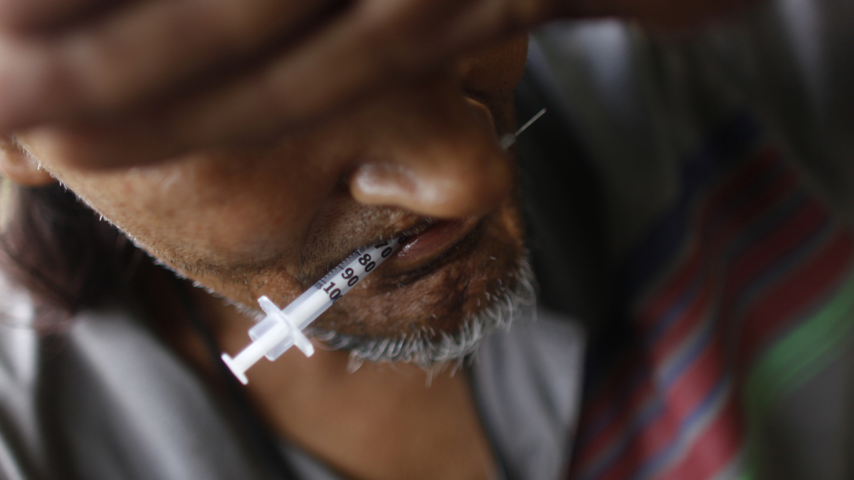  A heroin addict holds a used syringe in his mouth after shooting up. (Brennan Linsley/AP file photo) 
