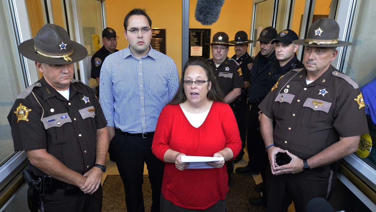  Surrounded by Rowan County Sheriff's deputies, Rowan County Clerk Kim Davis, center, with her son Nathan Davis standing by her side, makes a statement to the media at the front door of the Rowan County Judicial Center in Morehead, Ky., Monday, Sept. 14, 2015. Davis announced that her office will issue marriage licenses under order of a federal judge, but they will not have her name or office listed. (AP Photo/Timothy D. Easley) 