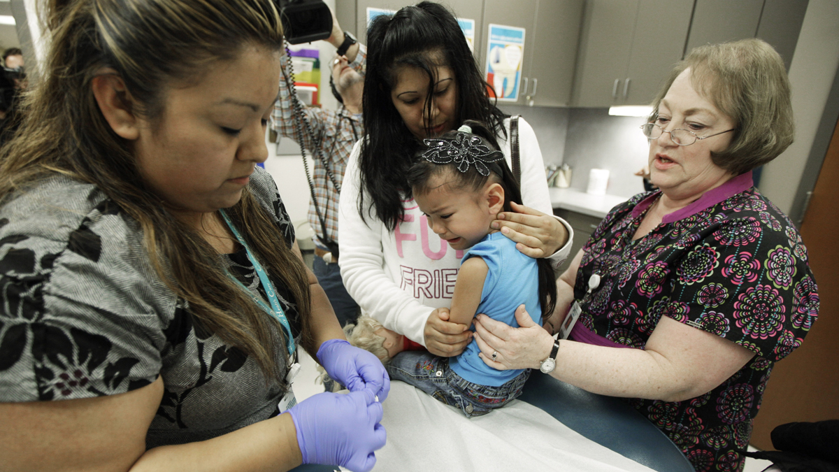 Nurses give a 4-year-old a whooping cough booster shot, as she is held by her mother at a health clinic (Ted S. Warren/AP Photo, file) 