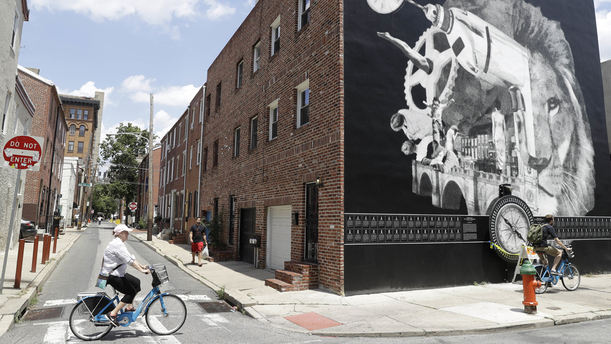 Cyclists move past a Philadelphia Mural Arts Program piece by New Orleans artist Candy Chang called “The Atlas of Tomorrow: A Device for Philosophical Reflections
