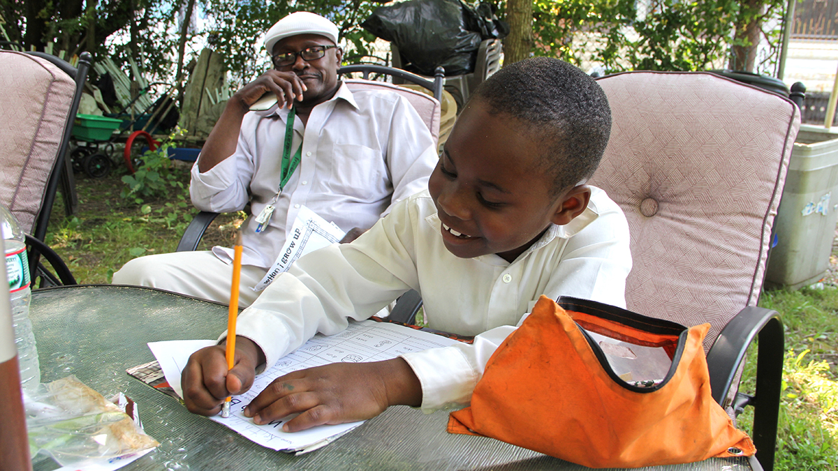 Keith Gray supervises his grandson's homework. Little Keith will be a first grader at Blaine Elementary this fall. (Emma Lee/WHYY) 