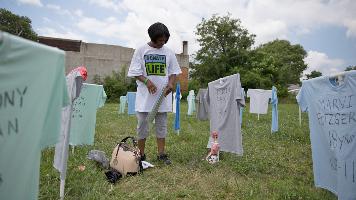  Carmen Johnson places a rose next to a T-shirt remembering her son, Rasheem who died Jan. 12, 2014.  The memorial, 144 T-shirts, mark the names of Chester residents who have died to gun violence in Chester, Pennsylvania since 2009.  (Lindsay Lazarski/WHYY)  