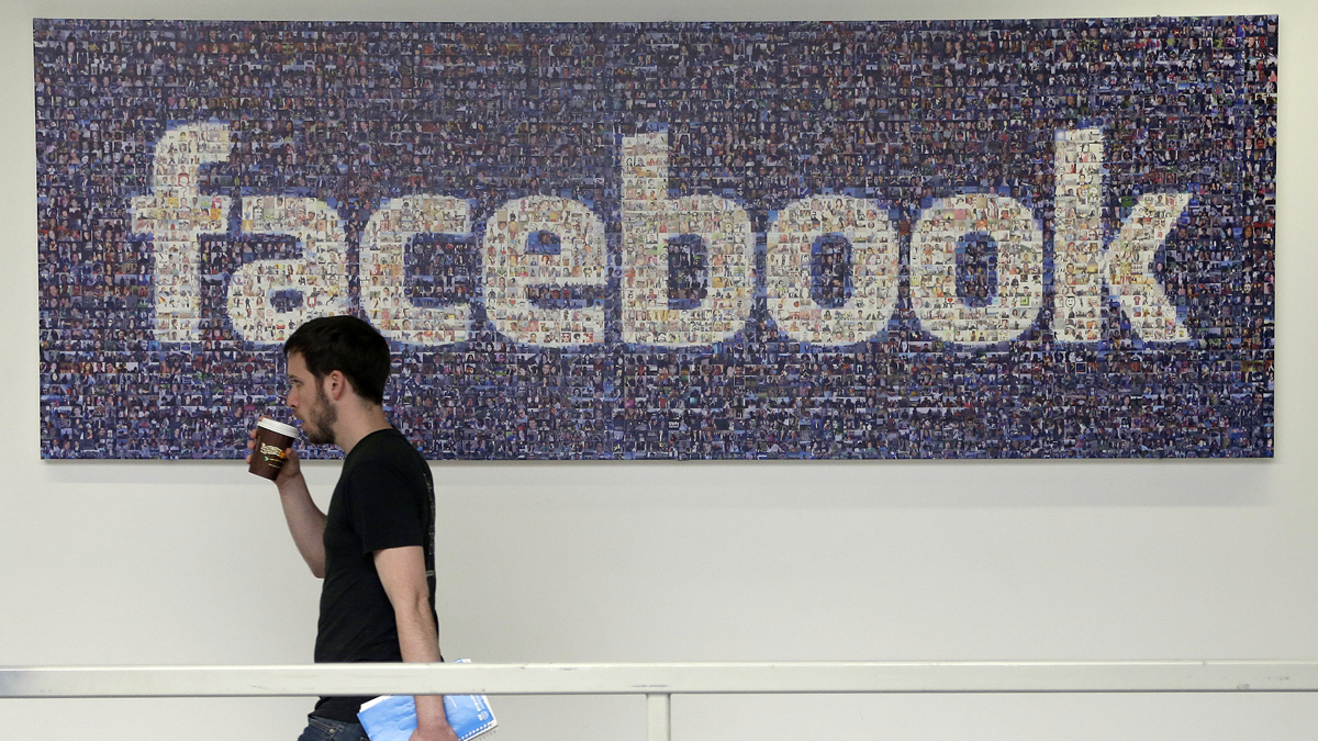A Facebook employee is shown walking past a sign at Facebook headquarters in Menlo Park