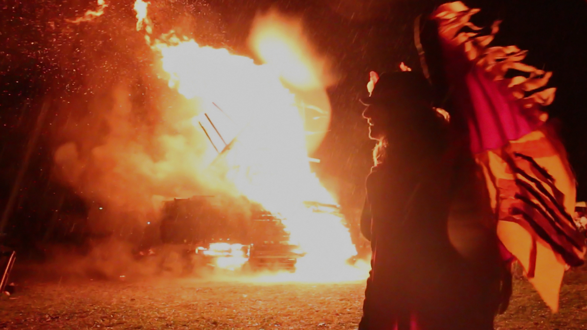  A woman dances in front of a giant wooden bird on fire at the annual Phoenixville Firebird Festival.  This year, vandals ignited the sculpture the night before the festival, but the community came together to build another bird. (Lindsay Lazarski/WHYY) 