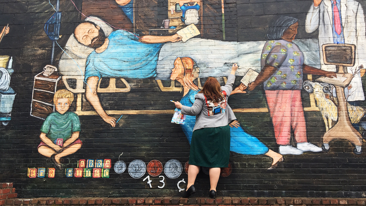Regina Holliday fixes up her first mural from 2009. It depicts her late husband and their tumultuous experience with health care. (Elana Gordon/WHYY)