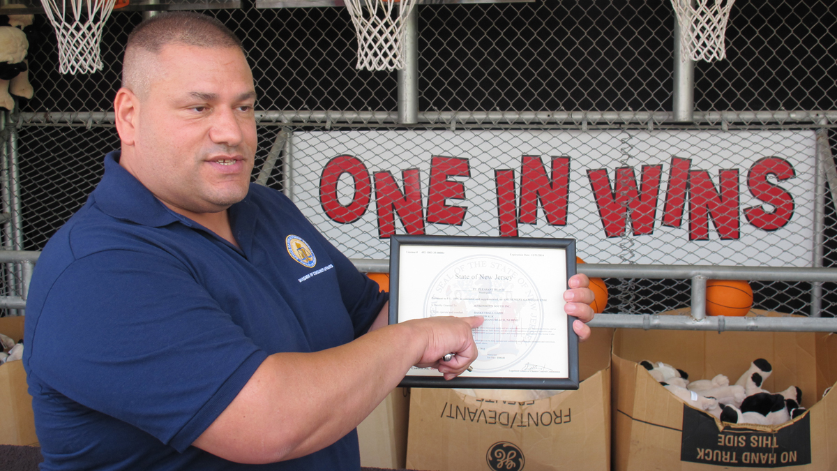  Joe Chessere, an investigator with New Jersey's Legalized Games of Chance Control Commission, examines the license at a basketball game stand on the Point Pleasant Beach boardwalk. (Phil Gregory/for WHYY) 
