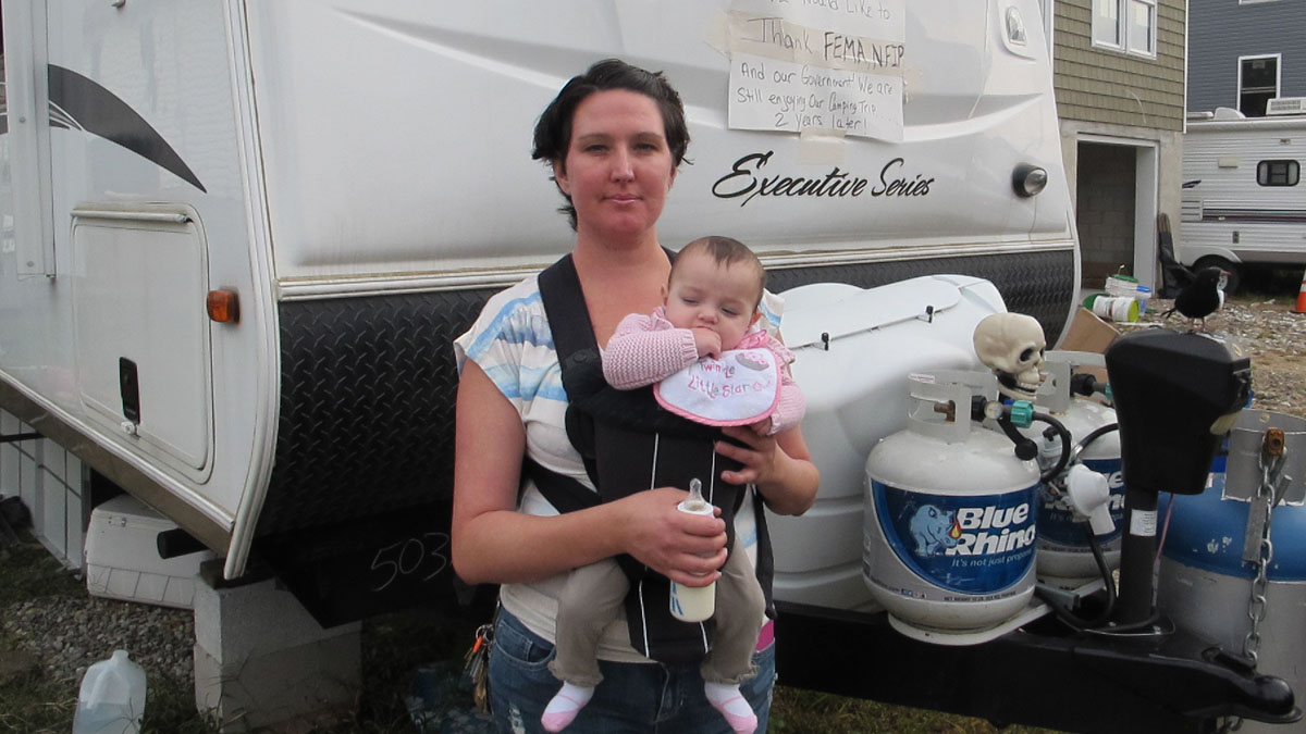  Andrea Kassimatis and her 6-month-old daughter stand in front of the trailer where the family is living next to their partially rebuilt home in Union Beach, New Jersey. (Phil Gregory/WHYY) 
