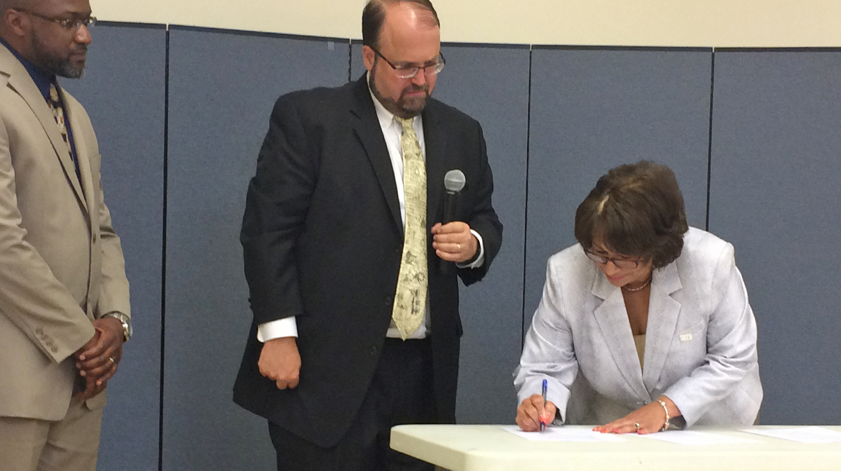 Harrisburg Mayor Eric Papenfuse (center) and Hamilton Health CEO Jeannine Peterson sign a memorandum of understanding for the new lead testing and abatement partnership. (Emily Previti/WITF)