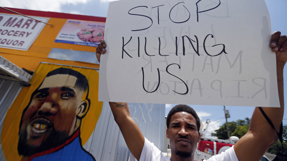 A man holds a sign in front of a mural of Alton Sterling while attorneys