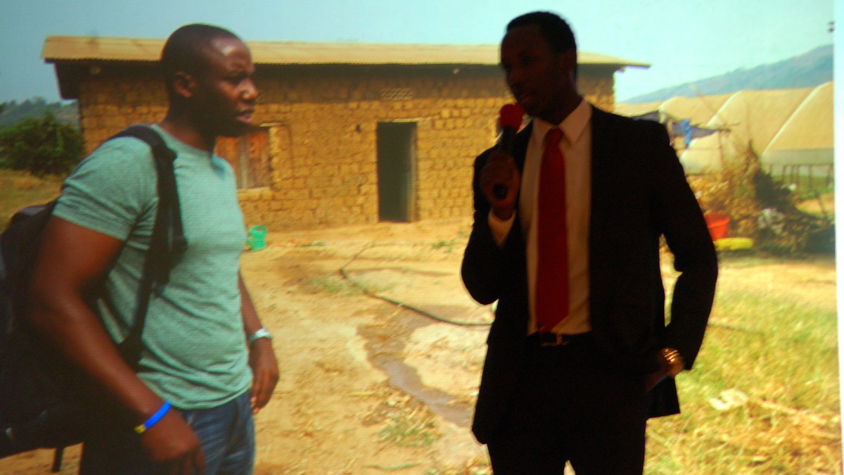  Emmanuel Habimana, stands next to a projected picture of himself visiting his native village. (Jon Campisi/for NewsWorks) 