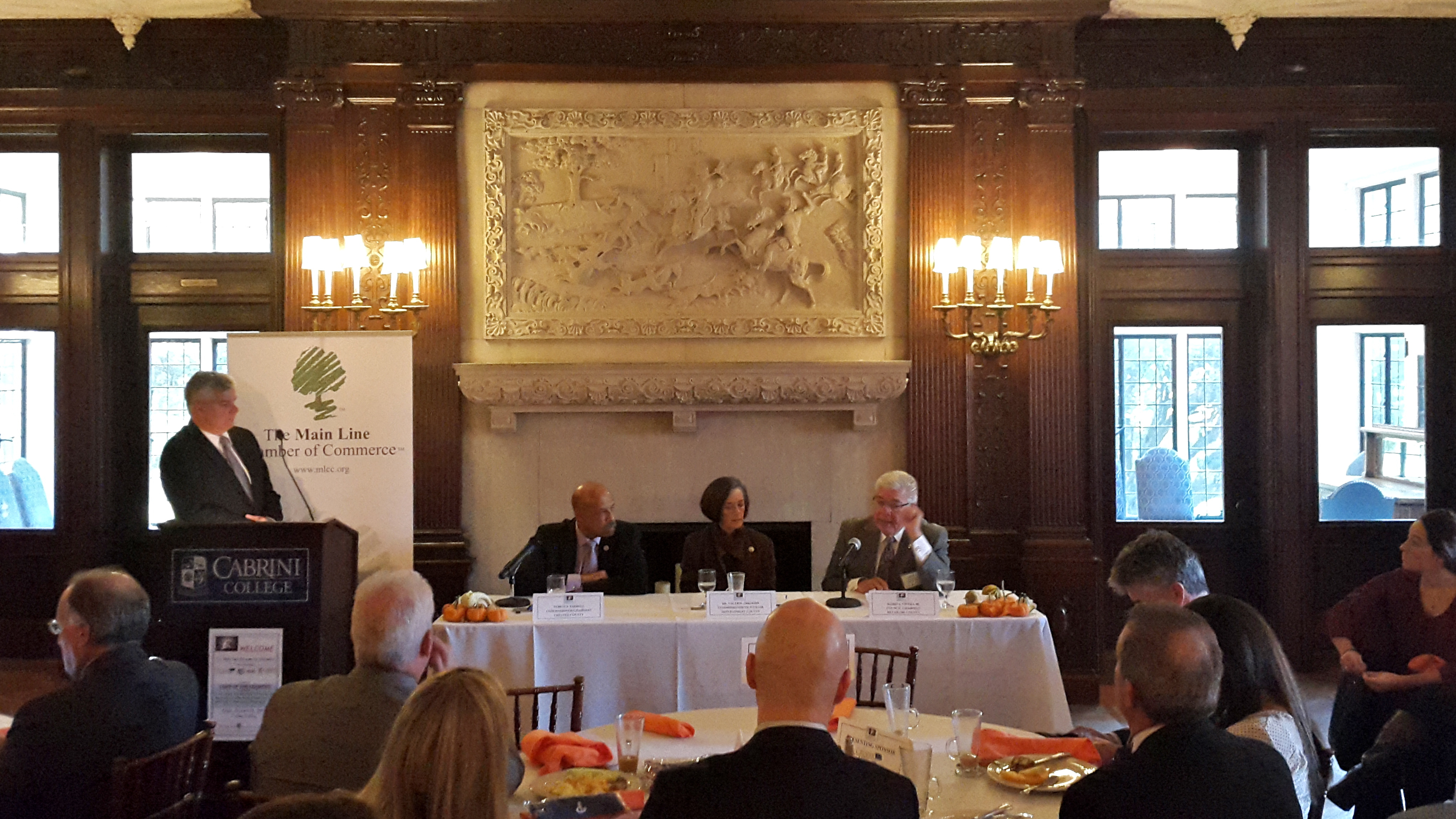  Delaware County Council chair Mario Civera (right) addresses the group at a State of the Counties meeting held by the Mainline Chamber of Commerce. Chair of the Chester County Board of Commissioners Terence Farrell (left) and Montgomery County Commissioner Val Arkoosh (center) said their counties have spent tens of millions of dollars to fulfill financial obligations since the budget impasse started in July.  (Laura Benshoff/WHYY) 