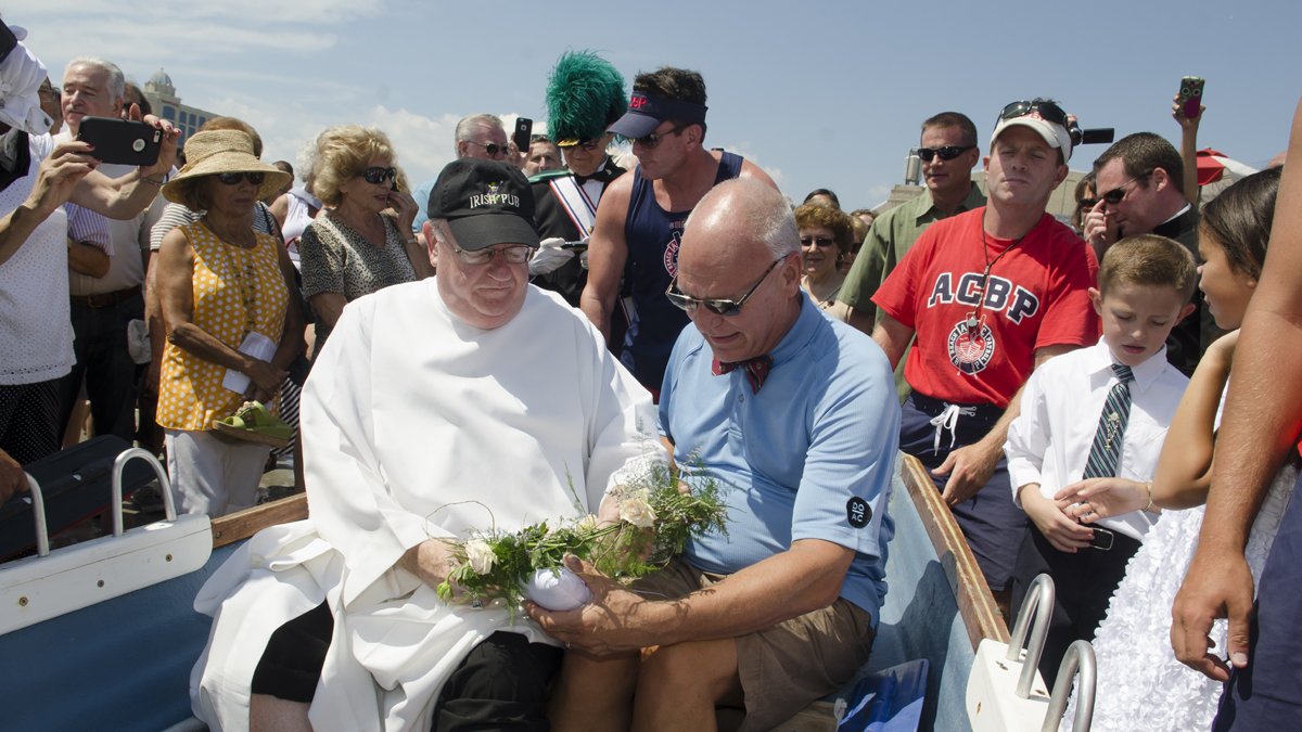 Bishop Dennis J. Sullivan and Atlantic City Mayor Don Guardian sit in an Atlantic City Beach Patrol rowboat and look over the ceremonial wreath and ring before being rowed away from shore to toss them into the ocean on Saturday, August 15, 2015. in celebration of the Wedding of the Sea. (Anthony Smedile/for NewsWorks) 