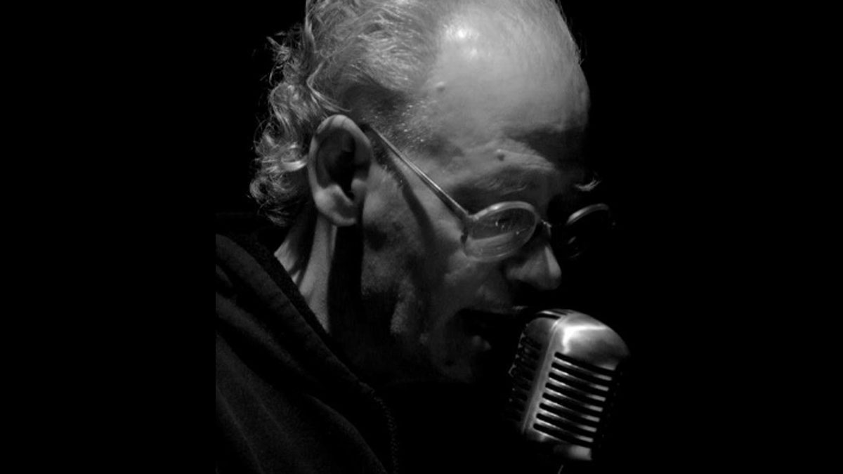  B&W photo of Marty Watt speaking into an old fashioned microphone. Valencia, Spain 2012. (Creative Commons via Wikipedia. Uploaded by Orsolya Lukács) 