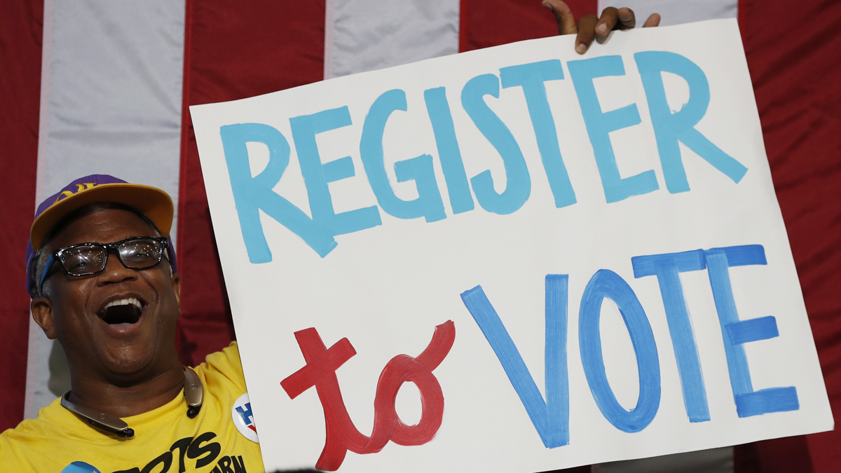 A man smiles while holding a sign that says, 