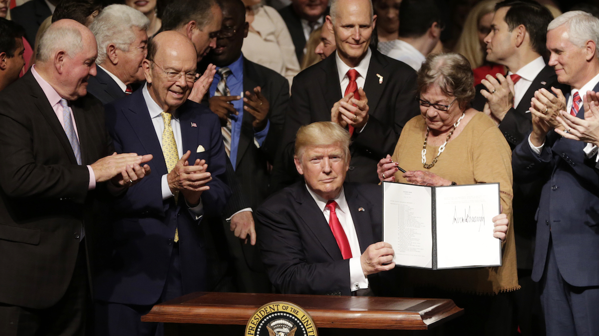  President Donald Trump shows the signed executive order surrounded by cabinet members and supporters in Miami, Friday, June 16, 2017. Trump announced a revised Cuba policy aimed at halting the flow of U.S. cash to the country's military and security services while maintaining diplomatic relations. From left are, Agriculture Secretary Sonny Perdue, Commerce Secretary Wilbur Ross, the president, Florida Gov. Rick Scott, Cary Roque, a Cuban political dissident, and Vice President Mike Pence. (AP Photo/Lynne Sladky) 