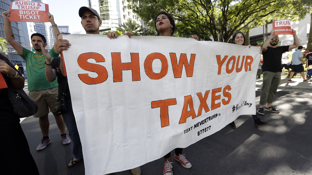 Protestors march in a downtown street holding a sign in support of Republican presidential candidate Donald Trump releasing his tax returns