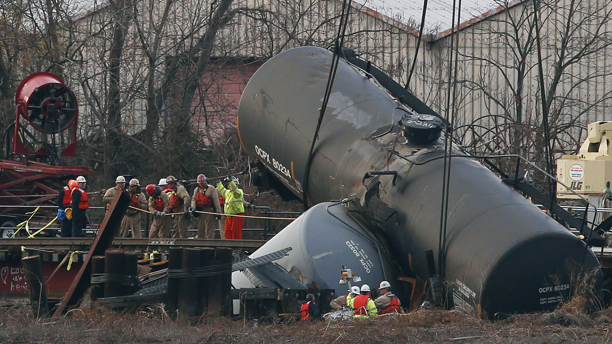 Workers secure lines around a train tank car as they prepare to pull it up with a crane from a crash site on a small bridge on the Mantua Creek
