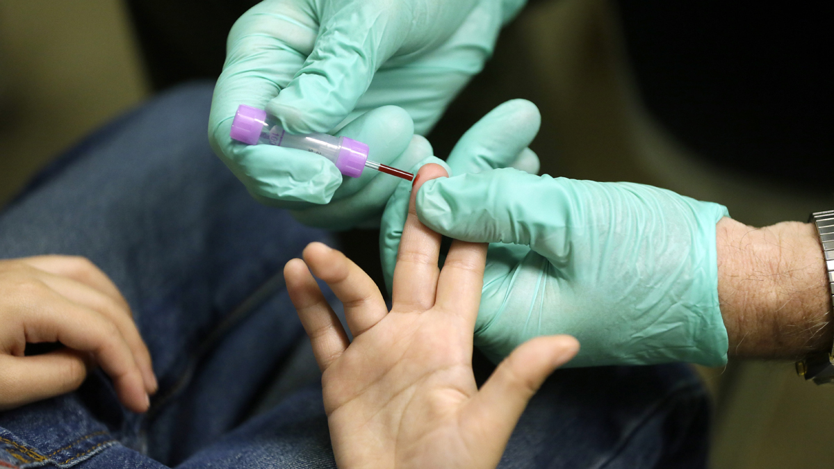 A certified medical assistant draws a blood sample from a child in Flint