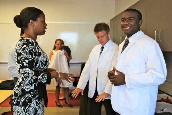 Medical students Heaton Kath and Imoh Ikpot and try their lab coats on for size with the help of staff member Marion Kyhna. (Emma Lee/for NewsWorks)