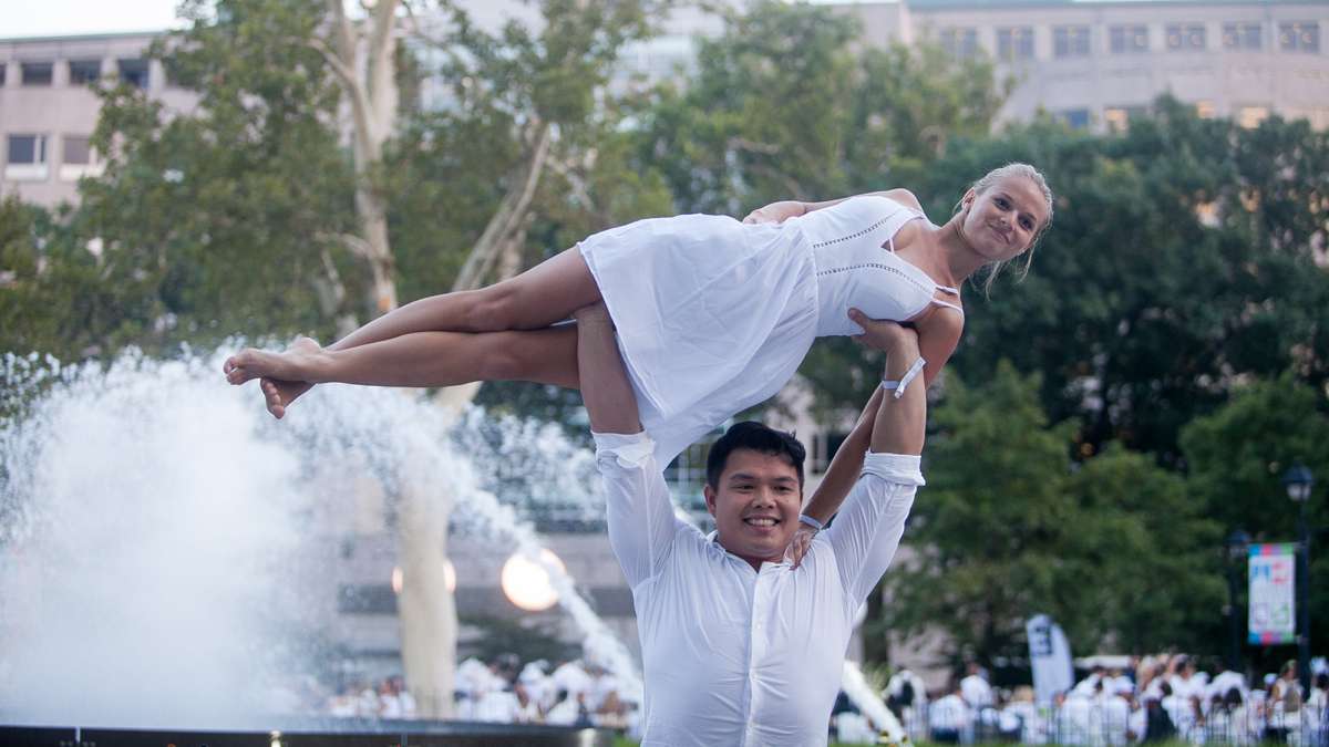 Acrobat Robert Li lifts Brittany Albertson near the Franklin Square fountain during Dîner en Blanc Thursday evening. (Brad Larrison for NewsWorks)