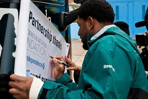 Philadelphia Eagles Player Akeem Jordan autographs a banner for Wister School on Tuesday after the Eagle Eyes Mobile made a stop to give eye checkups to uninsured or under-insured students. (Brad Larrison/for NewsWorks)