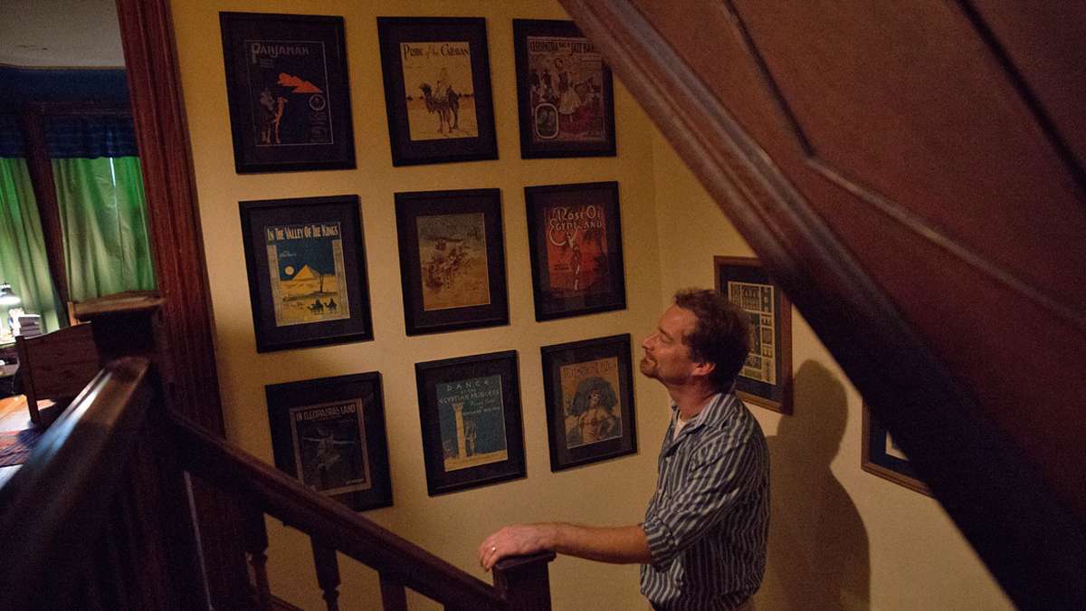 Josef Wegner walks past framed Egyptian themed sheet music.  (Lindsay Lazarski/WHYY)