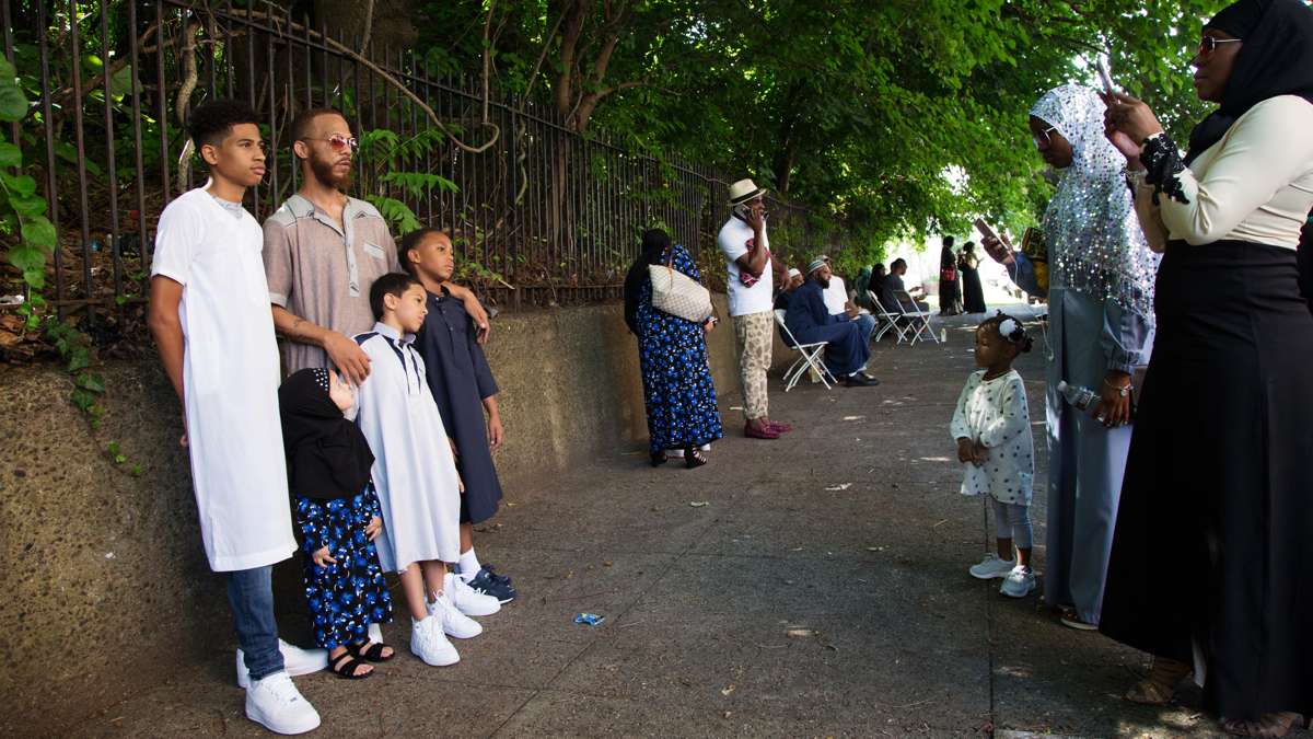 A woman takes a picture of a family on the sidewalk in front of Philadelphia Masjid