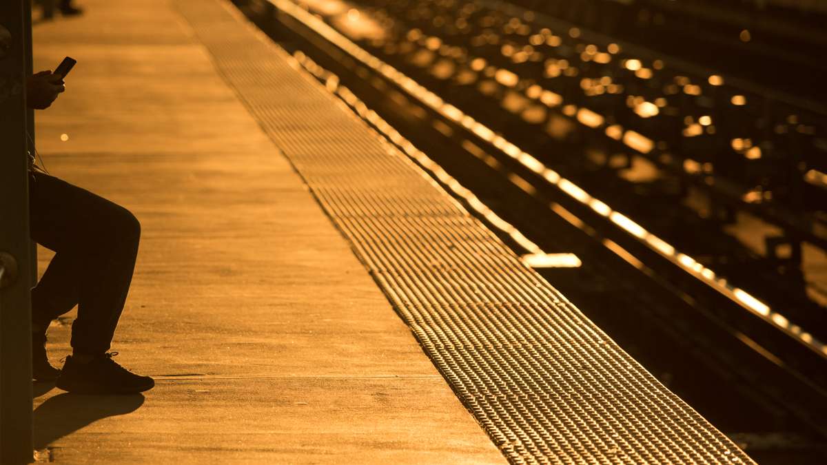 Yellow sunlight silhouettes a person waiting for a train on the Market Frankford El and causes the tracks to sparkle