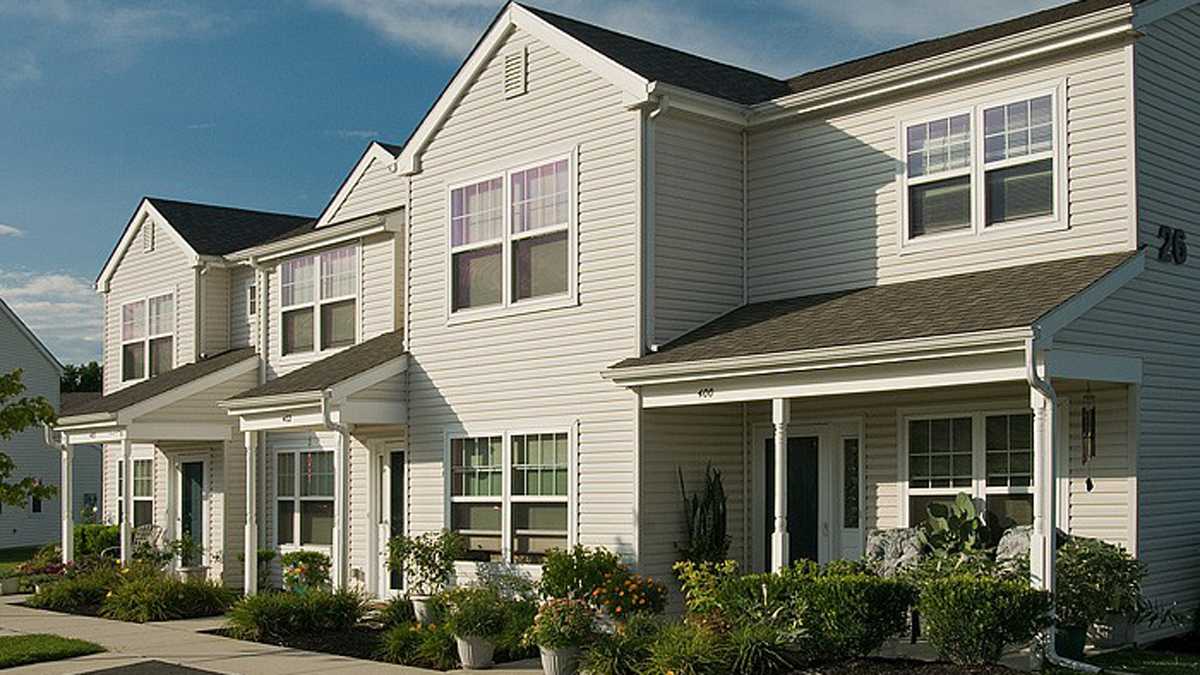 A row of suburban townhomes; vinyl siding, shrubs, and blue skies