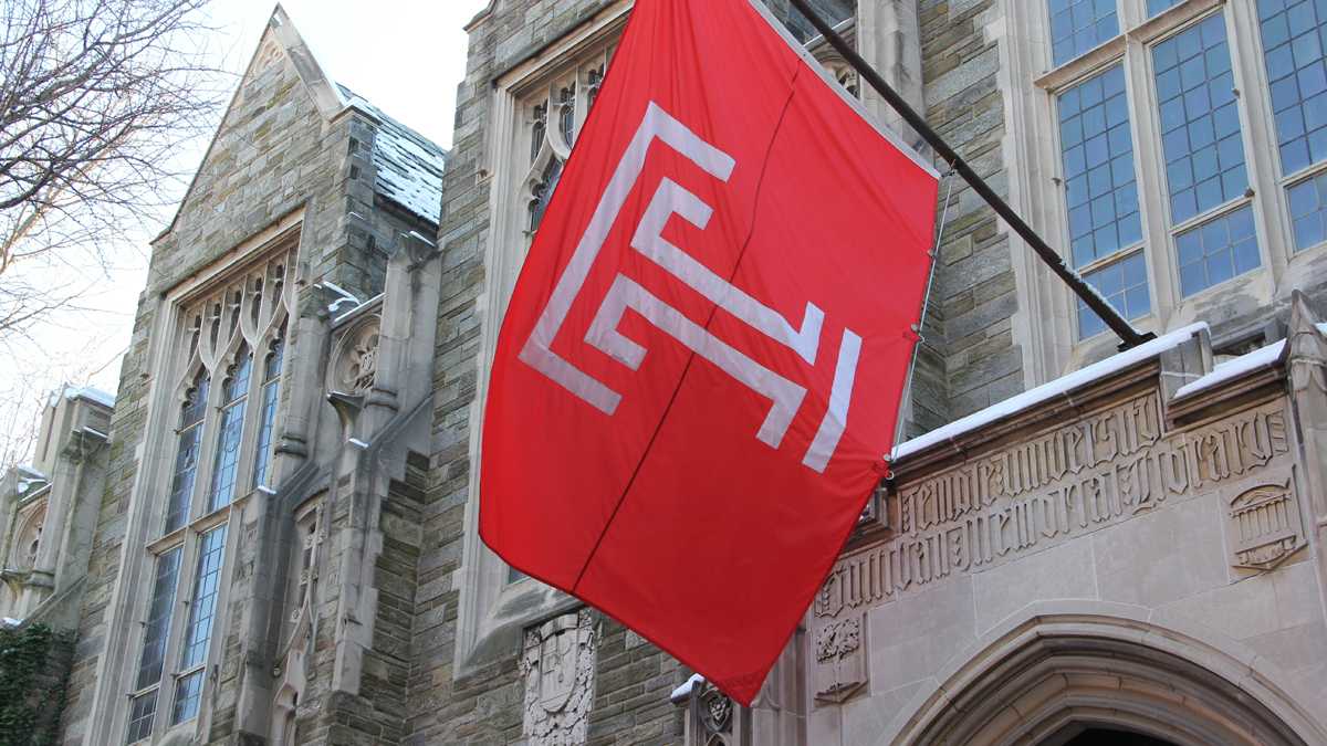 Cherry and white Temple University flag hangs outside of old stone buildings