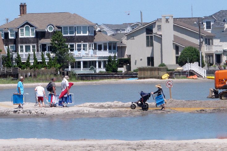  Beachgoers cross over one of numerous large pools of water that have formed on the beach in Margate N.J. due to heavy rains, Monday July 31, 2017. The water is blocked from draining into the ocean by new sand dunes being built as part of a storm protection program that Margate residents vigorously fought, claiming that the dunes would cause exactly the type of standing water that has occurred. (AP Photo/Wayne Parry) 