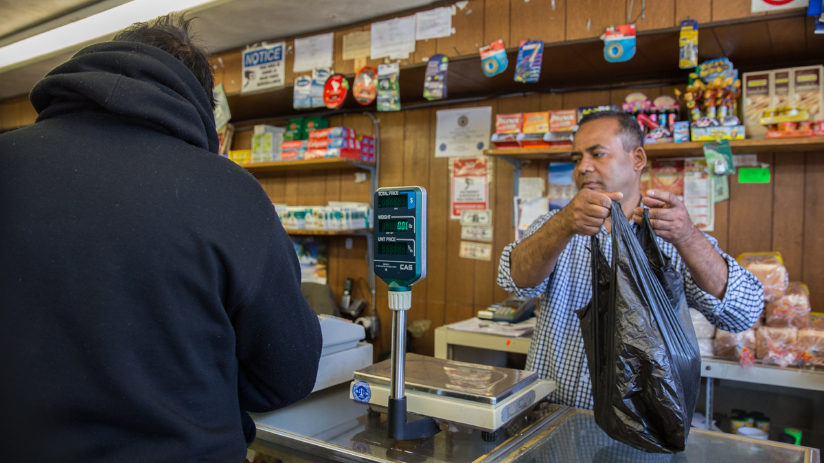  Mohammad J. Alam helps a customer at J&J Grocery store in Millbourne. With Sears gone, a handful of small businesses including the grocery store, beauty salons, smoke shops and an auto parts and accessory store bring in tax revenue for the borough. (Lindsay Lazarski/WHYY) 