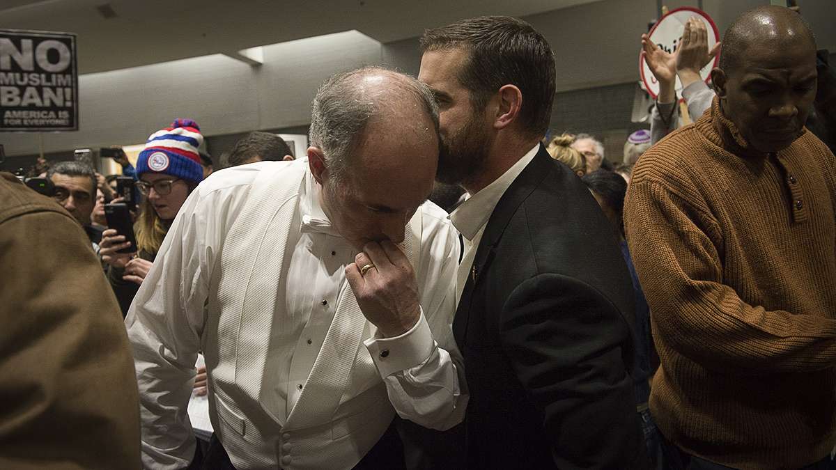 Senator Bob Casey gets a brief message from Representative Brina Sims while speaking to press and protesters at Philadelphia International Airport. (Branden Eastwood for NewsWorks)