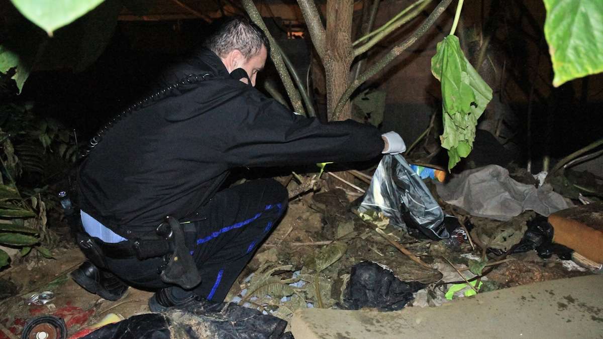 After apprehending a robbery suspect on the 2300 block of Franklin Street, officer James O'Neill combs through a vacant, looking lot for something a neighbor saw the boy stash a few moments before. (Kimberly Paynter/WHYY)