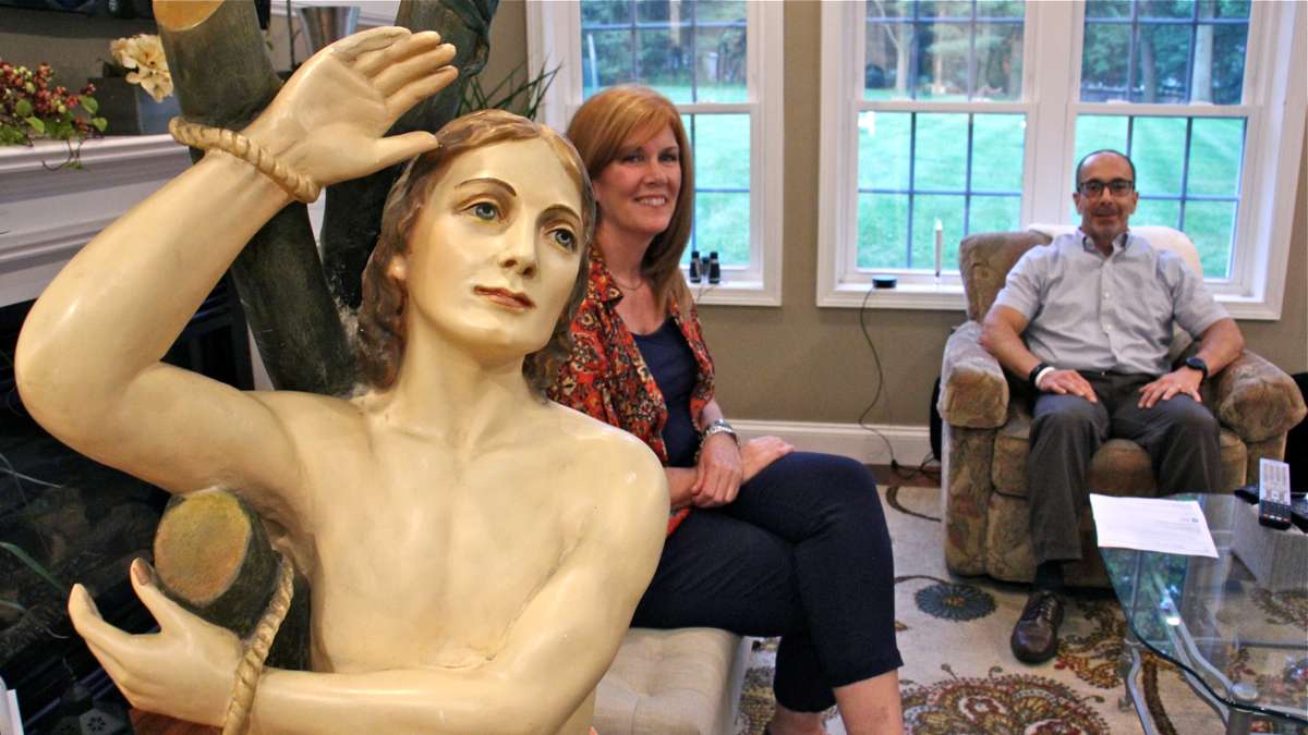 Ed and Kathleen Nader sit in their living room with a statue of St. Pantaleone that has been in Ed's family for four generations. (Emma Lee/WHYY)