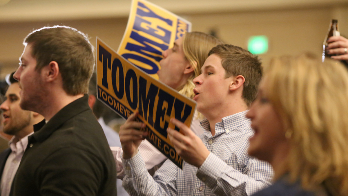  Leslie Springob (center) and Kean McLelland (center left), students at Kutztown University,  celebrate as the  GOP incumbent Pat Toomey is declared the winner in Pennsylvania’s U.S. Senate race. (Lindsay Lazarski/WHYY)  