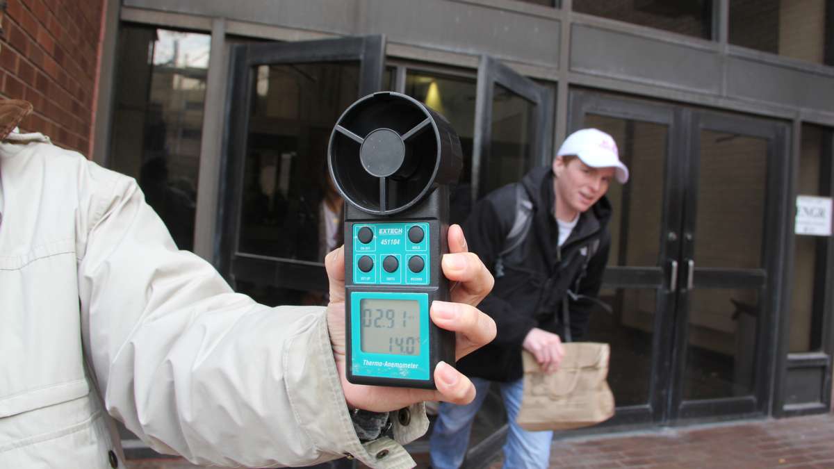 A Temple graduate student uses an anemometer to take a wind reading outside Temple's College of Engineering. (Emma Lee/WHYY)