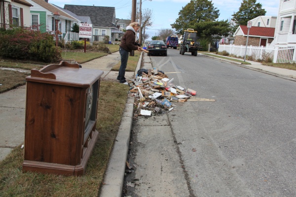 <p>In Margate, a woman tosses a few more books onto the pile of damaged possessions from her parents' house. (Emma Lee/for NewsWorks)</p>
